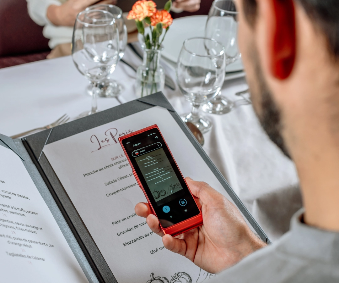 en mand i en elegant restaurant, der oversætter menuen ved hjælp af en fototranslator i en elektronisk oversætter