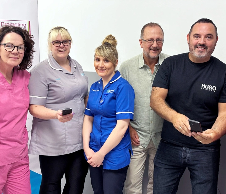 Fem smilende mennesker står sammen i sundhedstøj, og to af dem holder et oversætterapparat.