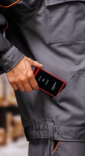 En person, der putter Vasco Translator Q1 i lommen – en kompakt enhed, der er kendt for sit batteri med lang levetid.