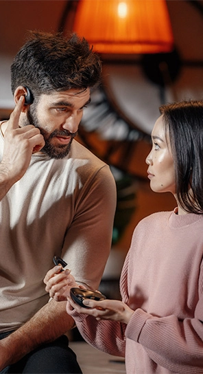 En mand med Vasco Translator E1-øretelefonen på, der står ved siden af en kvinde, der holder E1-enheden, og viser dens kraftfulde højttalere og smarte mikrofon frem.